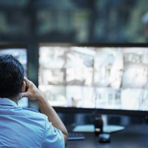 Security guard in control room, man checking cctv screen in surveillance office for building safety
