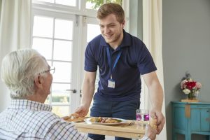 Male care worker serving dinner to a senior man at his home